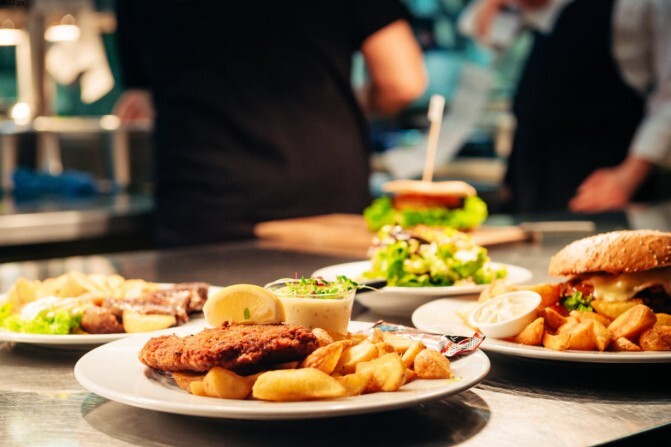 Mehrere fertig angerichtete Teller mit Schnitzel und Burger stehen am Küchenpass